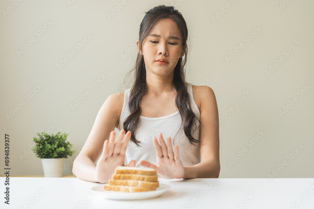 Gluten allergy, asian young woman hand push out, refusing to eat white bread slice on plate in breakfast food meal at home, girl having a stomach ache. Gluten intolerant and Gluten free diet concept. Gluten allergy, asian young woman hand push out, refusing to eat white bread slice on plate in breakfast food meal at home, girl having a stomach ache. Gluten intolerant and Gluten free diet concept.
