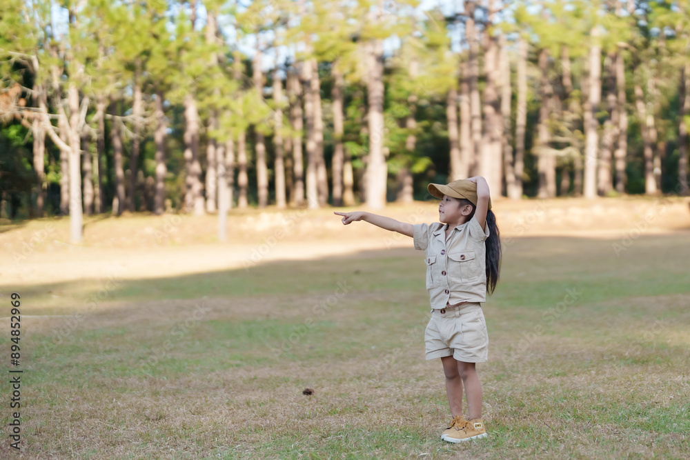 Asian girl in beige shorts and cap pointing with arm raised in park. Sunlit forest background, showing excitement and curiosity. Concept of exploration, adventure, and outdoor fun. Asian girl in beige shorts and cap pointing with arm raised in park. Sunlit forest background, showing excitement and curiosity. Concept of exploration, adventure, and outdoor fun.