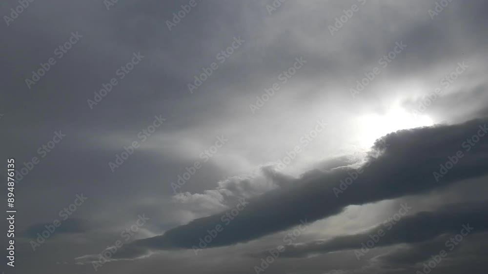 Cloudy grey sky with slowly moving Stratocumulus lenticularis clouds, sunlight and plane in flight with white line trace on winter day - natural sky background. Topics: weather, meteorology