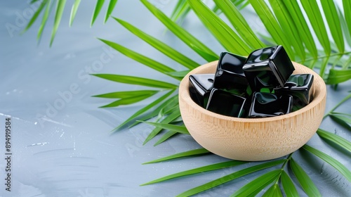 A wooden bowl filled with grass jelly cubes, surrounded by green leaves. Traditional Asian dessert and refreshment concepts. photo