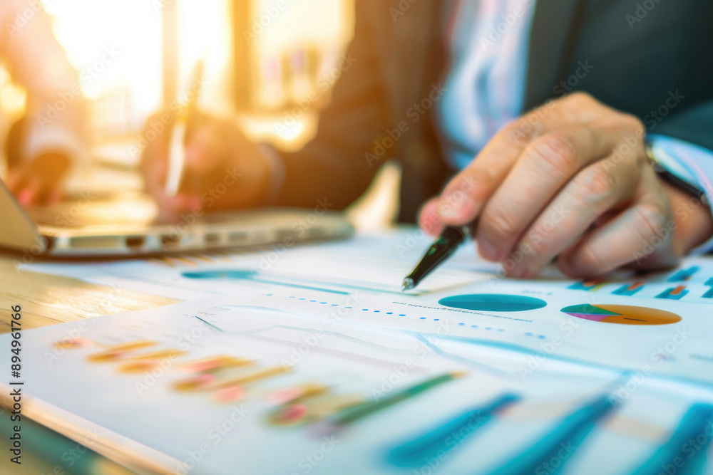 A business professional analyzing data charts and graphs with a laptop and pen in a bright office environment. A business professional analyzing data charts and graphs with a laptop and pen in a bright office environment.