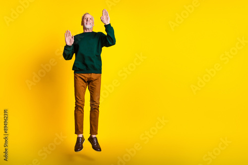 Full size photo of nice senior man jump touch wall mime dressed stylish green clothes isolated on yellow color background