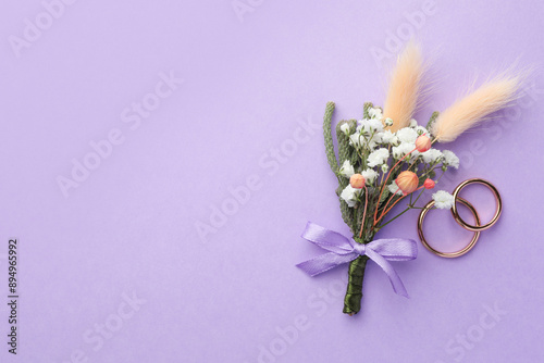 Small stylish boutonniere and rings on violet background, flat lay. Space for text photo