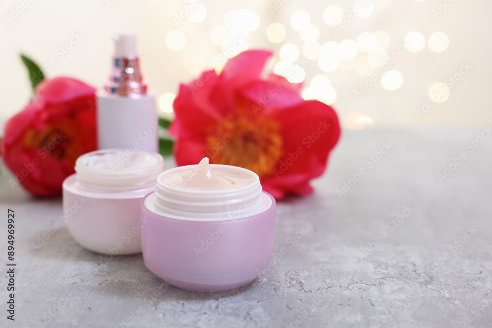 Set of different cosmetic products and peony flower on gray table against light background with blurred lights. Space for text Set of different cosmetic products and peony flower on gray table against light background with blurred lights. Space for text