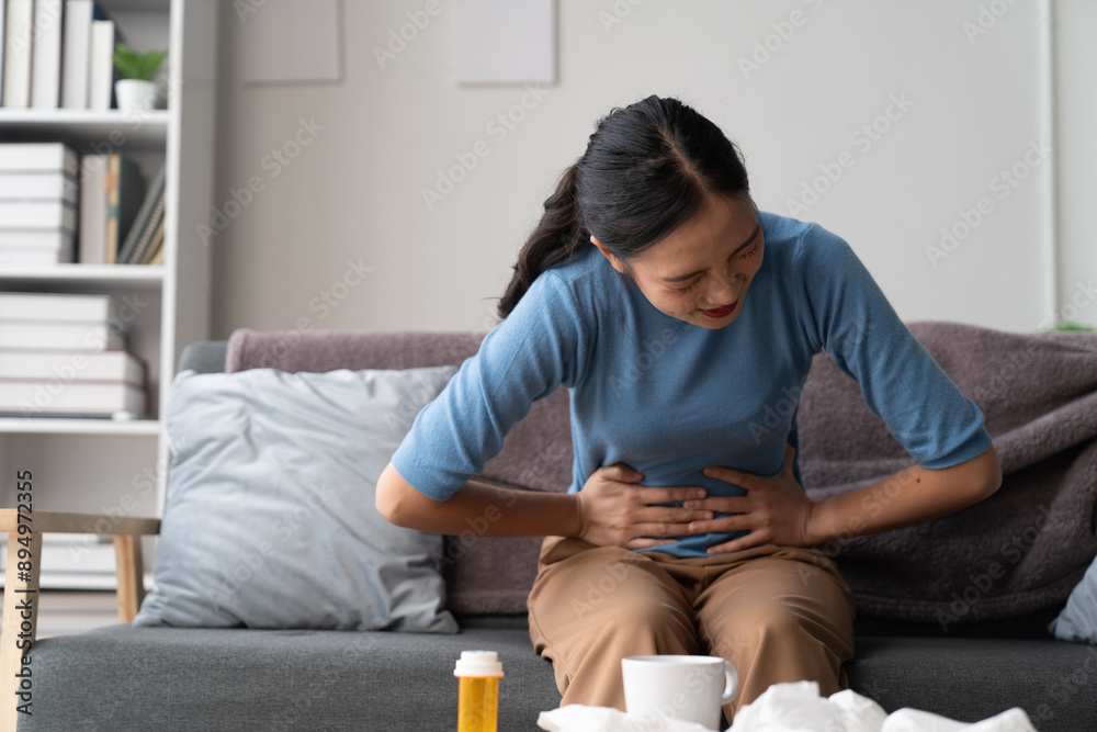A photograph depicting a female individual in a state of discomfort seated upon a sofa within a residential setting.