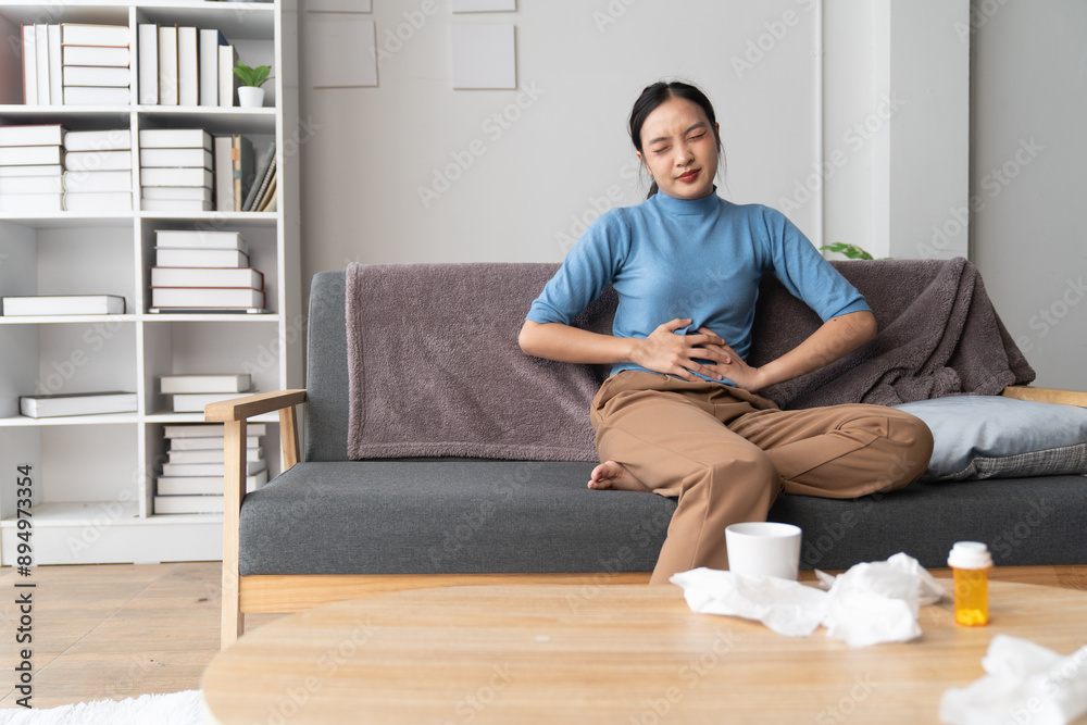 A photograph depicting a female individual in a state of discomfort seated upon a sofa within a residential setting.
