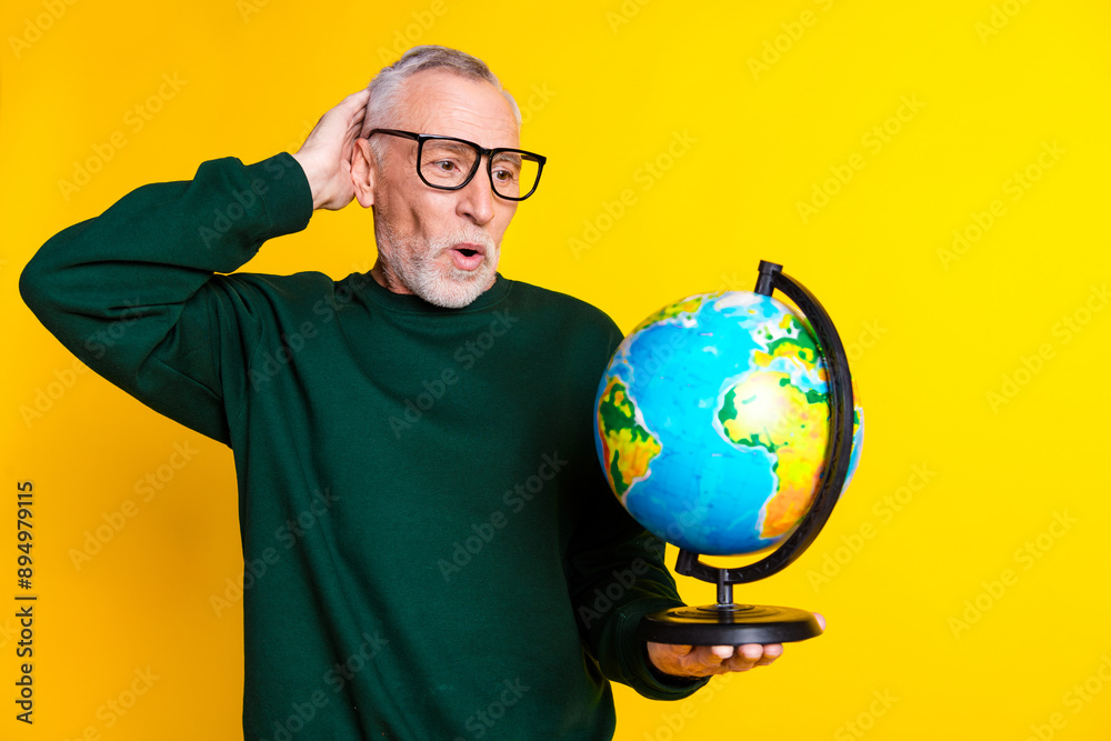 Photo portrait of nice senior man look nervous globe dressed stylish green clothes isolated on yellow color background Photo portrait of nice senior man look nervous globe dressed stylish green clothes isolated on yellow color background