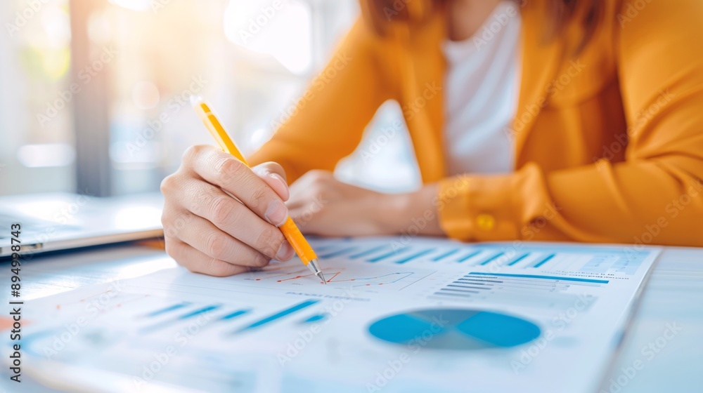 A woman is writing with a yellow pencil on a piece of paper. The paper has a lot of graphs and numbers on it. The woman is focused on her work and seems to be in a serious mood A woman is writing with a yellow pencil on a piece of paper. The paper has a lot of graphs and numbers on it. The woman is focused on her work and seems to be in a serious mood