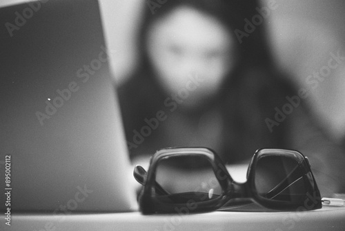 the girl is working on a laptop in the office, and her sunglasses are in the foreground