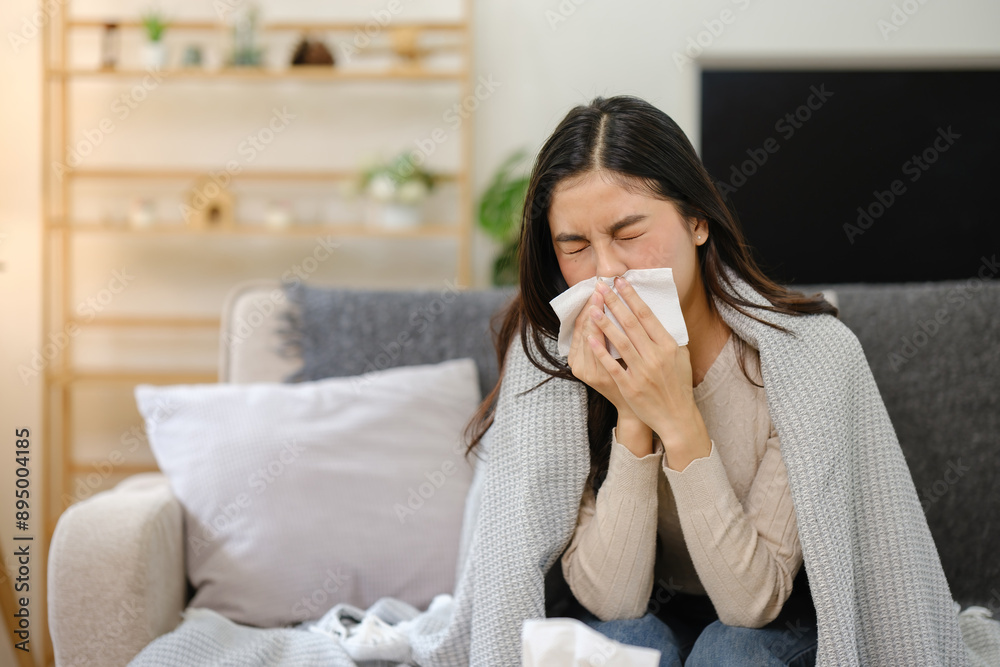 A woman is sitting on a couch with a tissue in her hand, covering her mouth A woman is sitting on a couch with a tissue in her hand, covering her mouth
