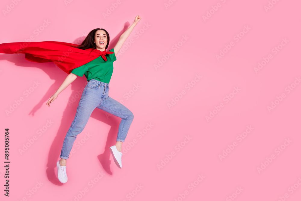 Full length photo of charming positive woman wear green t-shirt superman cape jumping high empty space isolated pink color background Full length photo of charming positive woman wear green t-shirt superman cape jumping high empty space isolated pink color background