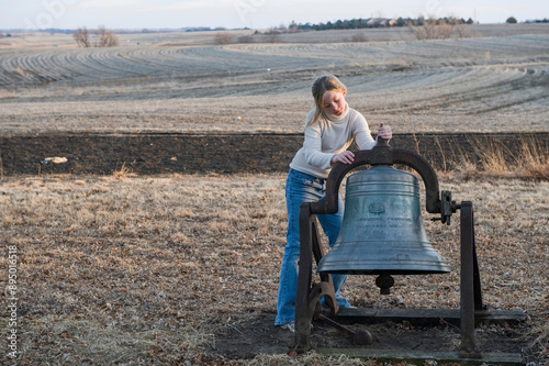 Girl stands by an old bell on farm in the vast counryside in Nebraska, USA; Cortland, Nebraska, United States of America photo