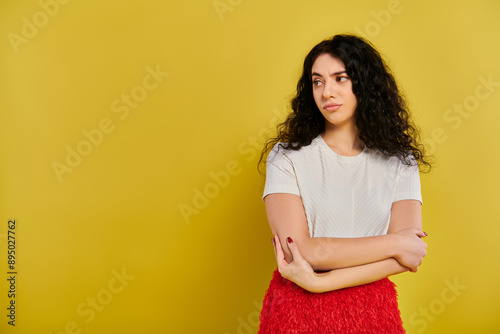 A stylish young woman with curly hair stands confidently with crossed arms against a vibrant yellow backdrop.