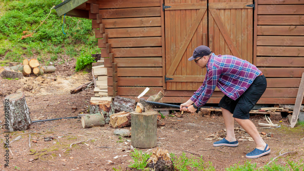 Male in shirt chopping wood with steel axe, country landscape with lumberjack, collecting firewood for winter. Wood shelter and forest on the background Male in shirt chopping wood with steel axe, country landscape with lumberjack, collecting firewood for winter. Wood shelter and forest on the background