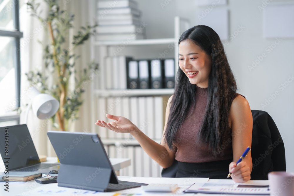 Manager is working from her home office, using a tablet to have a video call. She is smiling and gesturing with her hand Manager is working from her home office, using a tablet to have a video call. She is smiling and gesturing with her hand