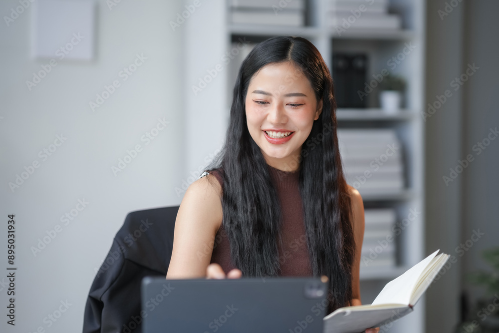 Focused asian businesswoman working on a tablet in a modern office, exuding professionalism and cheerfulness. Natural light creates a warm, inviting work environment Focused asian businesswoman working on a tablet in a modern office, exuding professionalism and cheerfulness. Natural light creates a warm, inviting work environment