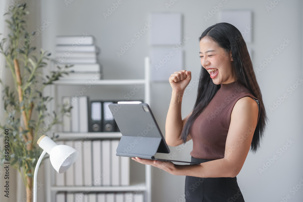 Asian businesswoman happily working in her office, celebrating success with a fist pump. She exudes confidence and determination, symbolizing ambition and leadership in the corporate world Asian businesswoman happily working in her office, celebrating success with a fist pump. She exudes confidence and determination, symbolizing ambition and leadership in the corporate world