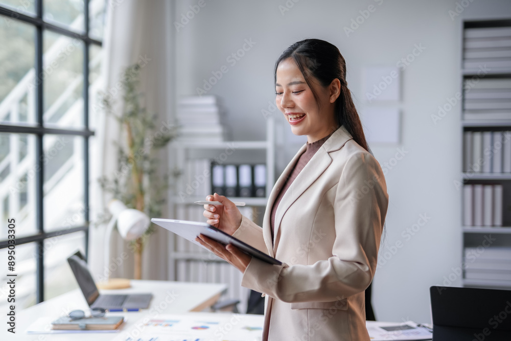 Businesswoman is analyzing data on a digital tablet while working in a bright office. She is smiling and appears to be enjoying her work Businesswoman is analyzing data on a digital tablet while working in a bright office. She is smiling and appears to be enjoying her work