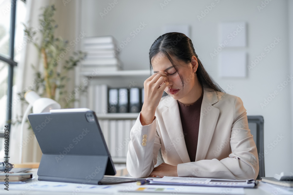 Stressed young businesswoman with a headache works on laptop in office, battling burnout and exhaustion from overwork and deadlines. Professional despite pain, analyzing finance documents Stressed young businesswoman with a headache works on laptop in office, battling burnout and exhaustion from overwork and deadlines. Professional despite pain, analyzing finance documents
