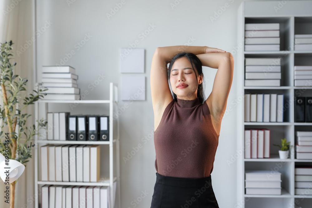 Young asian businesswoman is taking a break from work to stretch her arms in her office. She is standing with her eyes closed, enjoying the moment of relaxation Young asian businesswoman is taking a break from work to stretch her arms in her office. She is standing with her eyes closed, enjoying the moment of relaxation