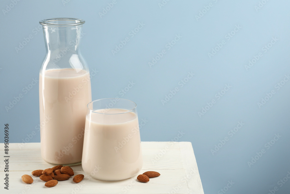 Fresh almond milk in carafe, glass and nuts on white wooden table, space for text Fresh almond milk in carafe, glass and nuts on white wooden table, space for text