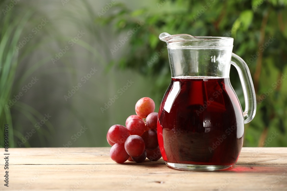 Tasty juice in glass jug and grapes on wooden table outdoors, space for text Tasty juice in glass jug and grapes on wooden table outdoors, space for text