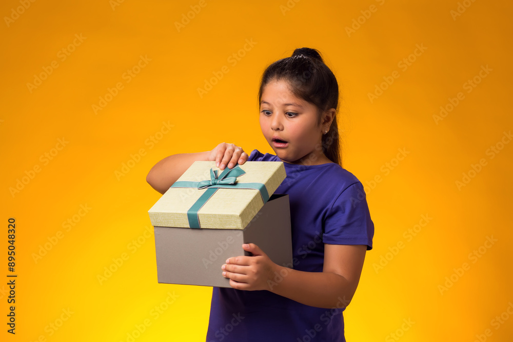 Smiling kid girl holding giftbox and looking inside the box over yellow background. Birthday and celebration concept Smiling kid girl holding giftbox and looking inside the box over yellow background. Birthday and celebration concept