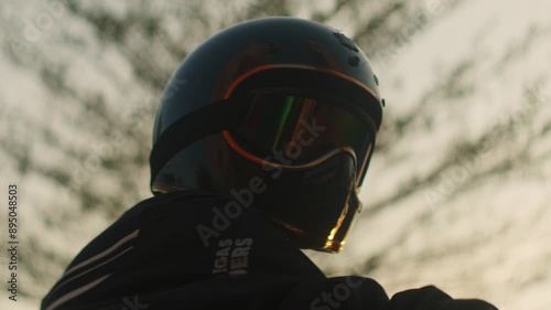 portrait of motorcycle rider biker wearing helmet and googles sunglasses standing proud at sunset during a road trip adventure holiday travel 