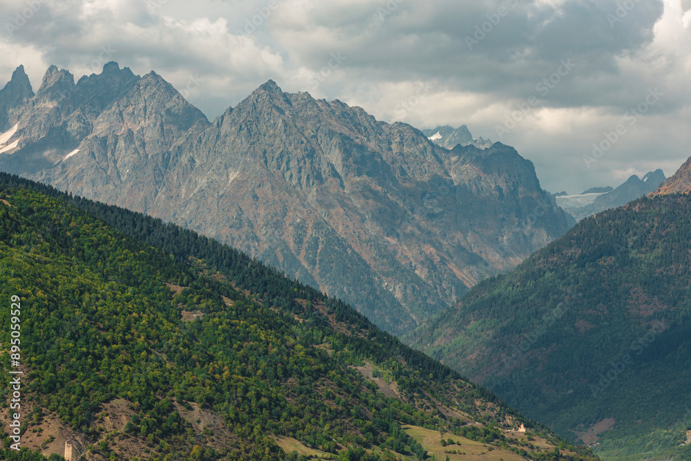 Forested mountainsides and rugged peaks of the Caucasus Mountains with dark clouds above; Hebudi, Svanteti, Georgia Forested mountainsides and rugged peaks of the Caucasus Mountains with dark clouds above; Hebudi, Svanteti, Georgia