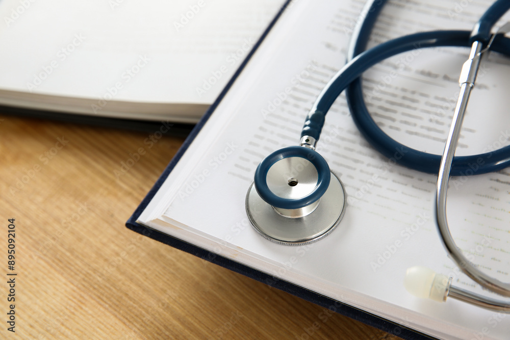 One new medical stethoscope and books on wooden table, closeup One new medical stethoscope and books on wooden table, closeup