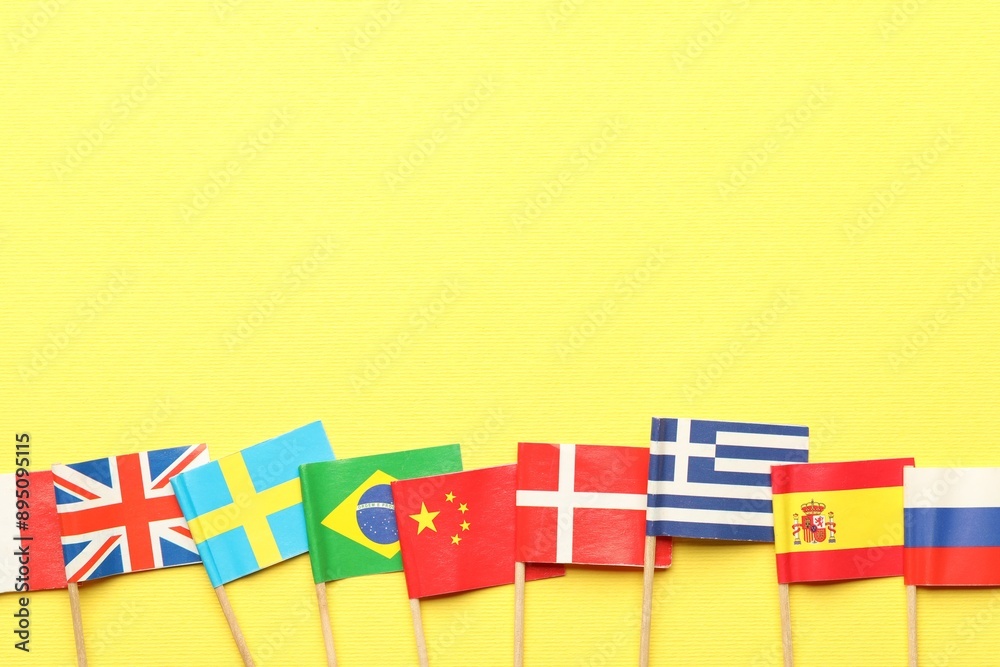 Obraz premium Small paper flags of different countries on yellow background, flat lay. Space for text