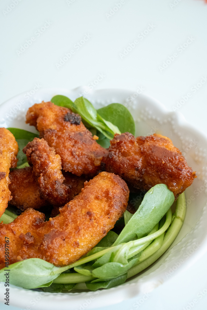 Fried chicken breast in bite-sized pieces with greens in a white bowl close-up Fried chicken breast in bite-sized pieces with greens in a white bowl close-up
