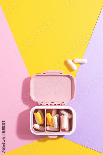 Creative medical and health care composition: open pill box with white and yellow capsules on colourful background. Daily medication and supplement management, health and wellness concept.