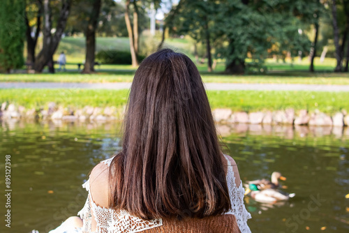 A woman is sitting in front of a lake filled with ducks photo