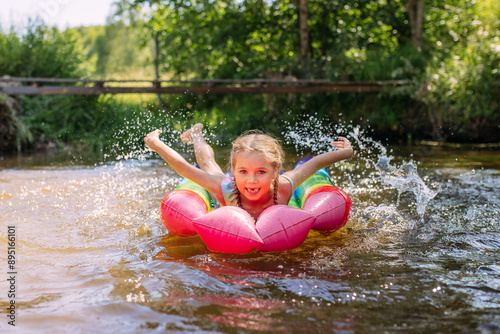 a girl child swims in the water of the river inflatable mattress laughter joy splashes summer heat