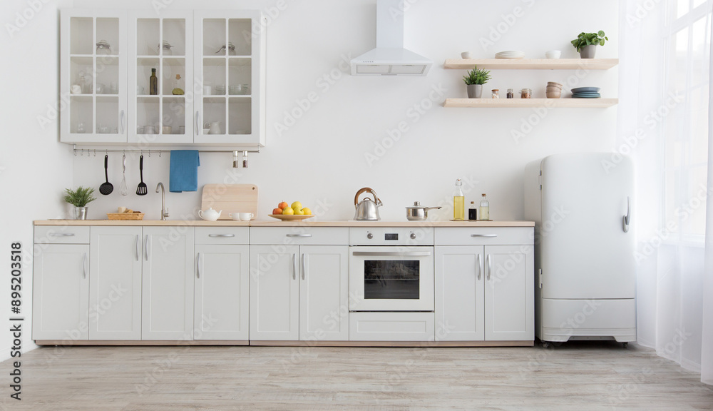 Fototapeta premium White scandinavian kitchen interior with dining room and wooden floor. Simply furniture with utensils, shelves with crockery and plants in pot, refrigerator in modern minimal design, empty space