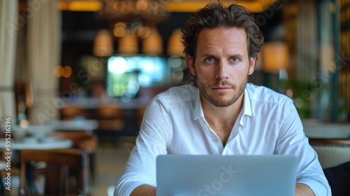 A young man is working on his laptop, possibly a freelancer or student. He is seated in a calm indoor setting, focused on his work.