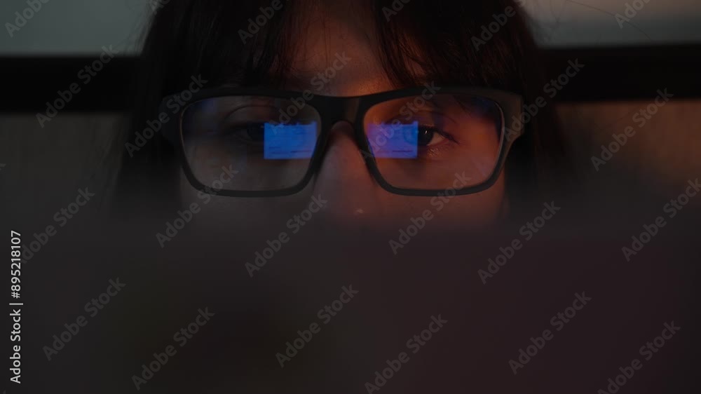 A young woman wearing glasses works at a computer in the evening. A young woman wearing glasses works at a computer in the evening.