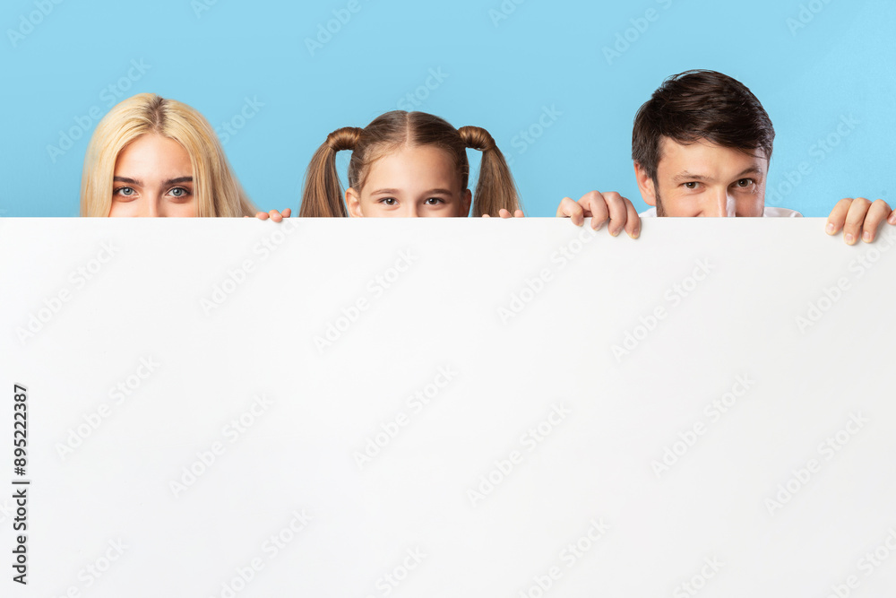 A family, consisting of a mother, father, and daughter, are peeking over a large white sign. They are smiling and looking at the camera. The background is a light blue color. A family, consisting of a mother, father, and daughter, are peeking over a large white sign. They are smiling and looking at the camera. The background is a light blue color.