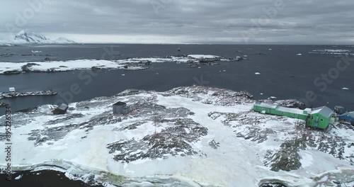 Polar station buildings on rocky island in Antarctica. Frozen coast, cold ocean, mountains in background. Winter wild nature landscape. Antarctic expeditions, travel. South Pole explore. Drone flight