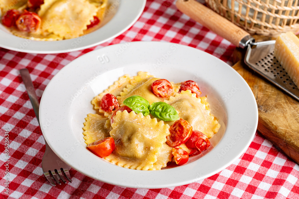 Creamy Italian Ravioli with tomatoes. Table with traditional red and white chess tablecloth. Creamy Italian Ravioli with tomatoes. Table with traditional red and white chess tablecloth.