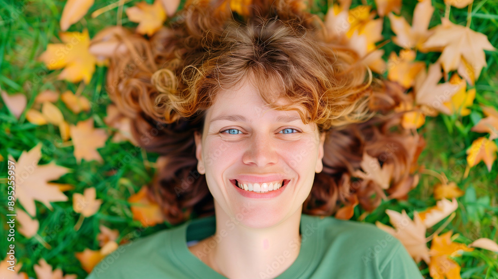 Smiling woman lying on the ground surrounded by autumn leaves. Happy woman enjoying a sunny day in autumn with vibrant foliage. Joyful expression in nature's beauty