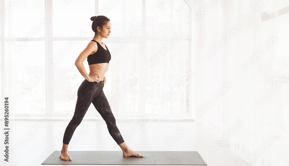 Fototapeta premium A woman dressed in a black top and leggings is standing confidently on a yoga mat, ready to begin her workout. She appears focused and determined as she prepares for her yoga practice.