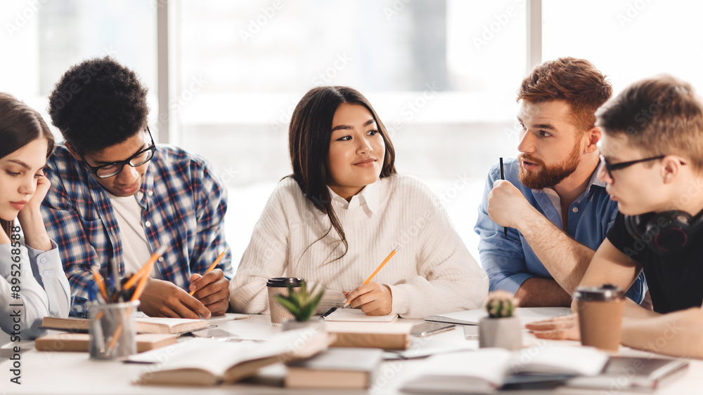 A diverse group of students sitting together at a table, engaged in conversation and possibly doing homework. Some are gesturing while speaking, while others are listening attentively A diverse group of students sitting together at a table, engaged in conversation and possibly doing homework. Some are gesturing while speaking, while others are listening attentively