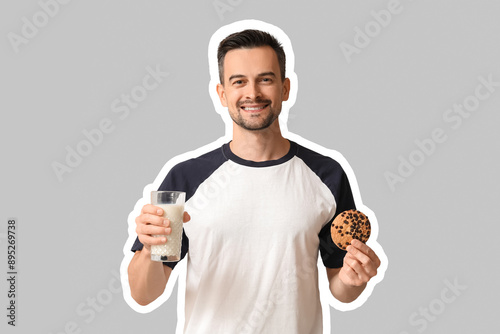 Handsome man with tasty cookie and glass of milk on grey background