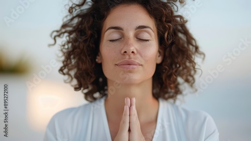 A woman meditates with her eyes closed, hands in prayer pose, enjoying the tranquility of an outdoor setting with soft lighting, representing peace and inner harmony.