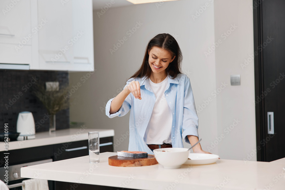 A woman in a blue shirt standing in a kitchen holding a bowl of food and smiling at the camera
