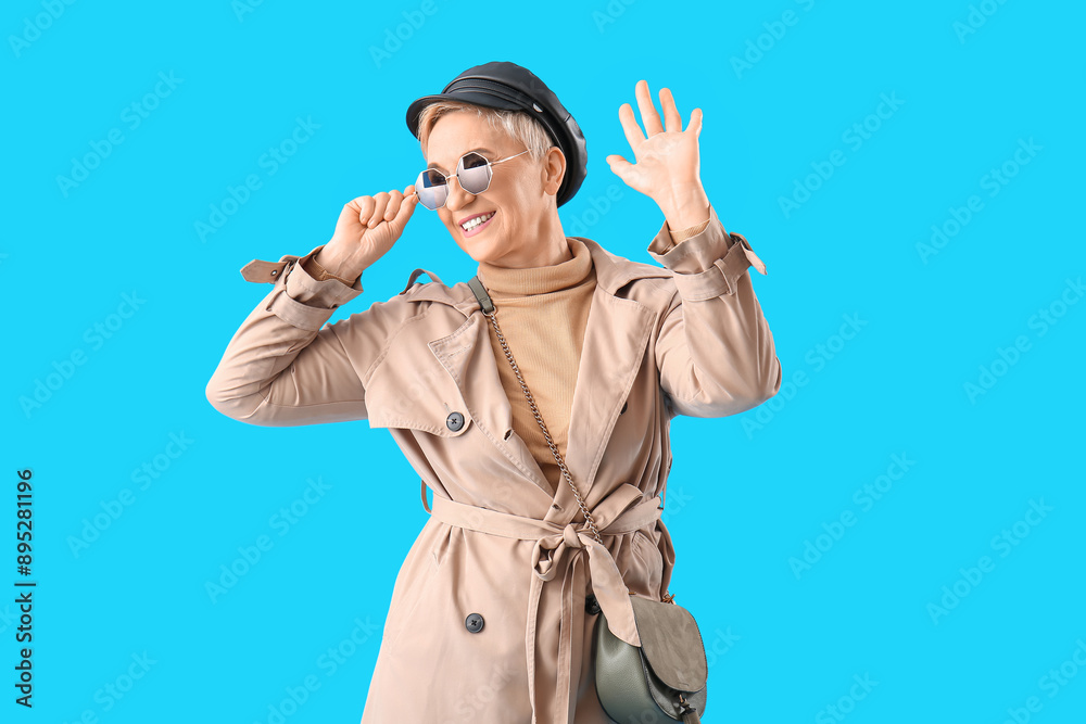 Stylish mature woman waving hand on light blue background Stylish mature woman waving hand on light blue background