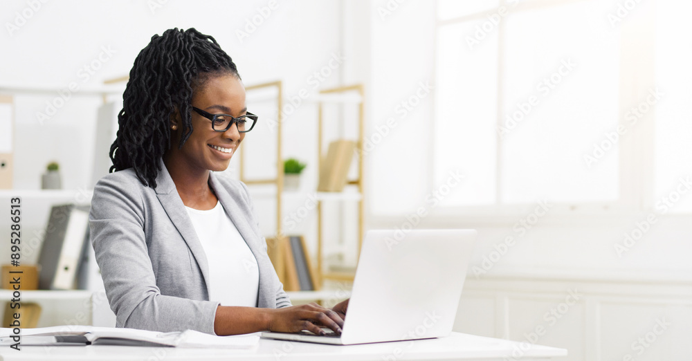 Positive African American businesswoman working at her desk with a laptop, writing notes in a modern office environment, copy space Positive African American businesswoman working at her desk with a laptop, writing notes in a modern office environment, copy space