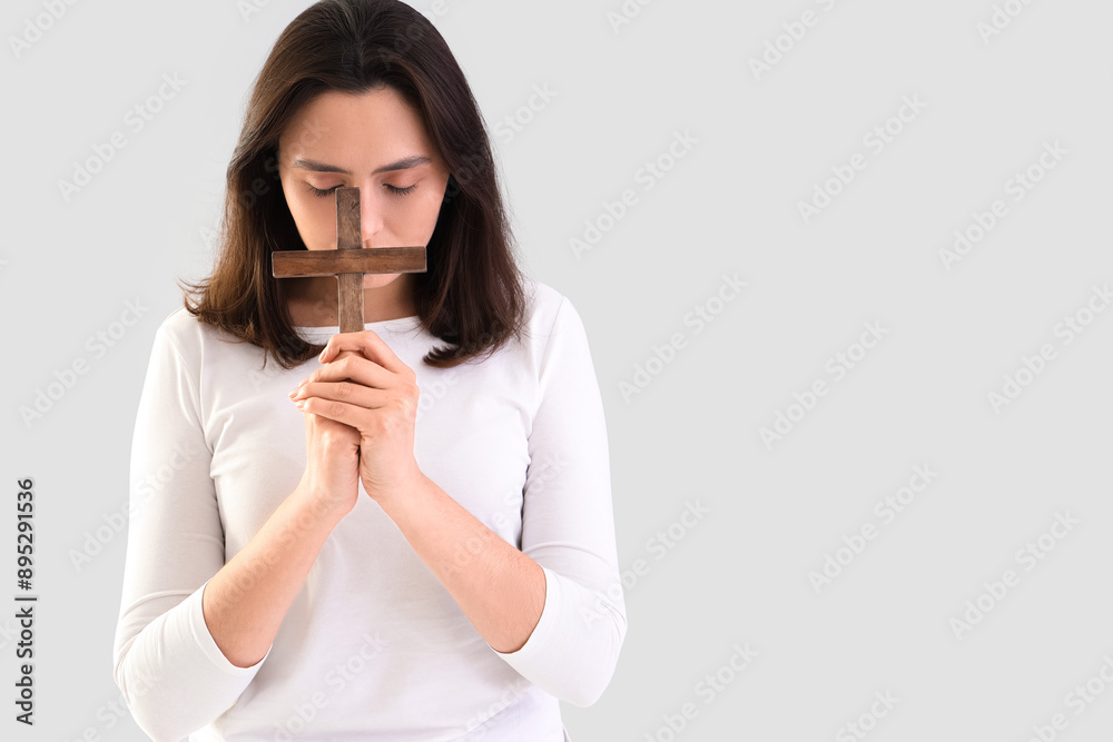 Young woman praying with cross on light background